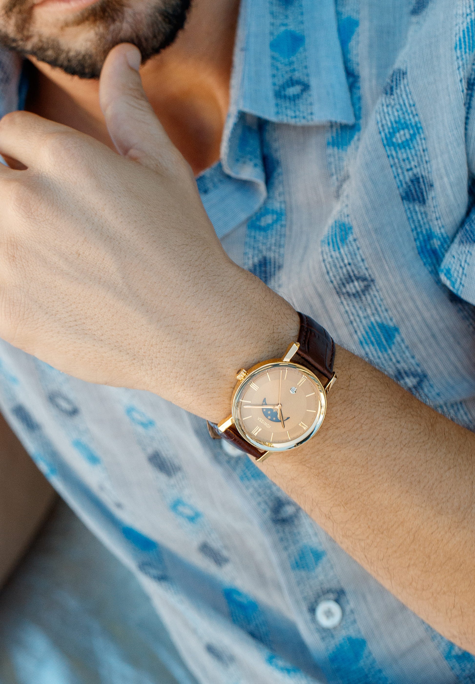 Brown swiss watch - with brown leather strap and gold dial with moon and stars details - all swiss made - worn by a man with blue t shirt