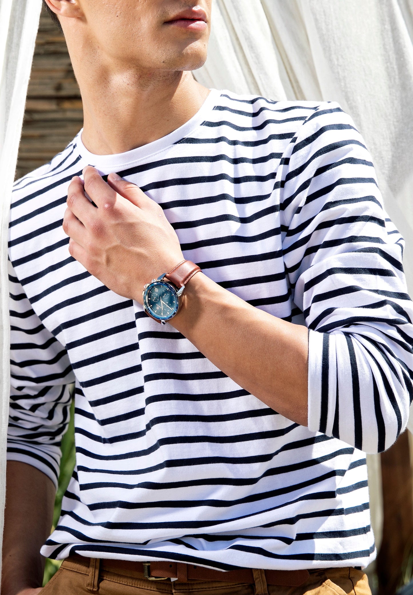 Brown swiss watch worn by a man who is wearing a white and blue shirt - the watch has brown leather strap and blue dial - all swiss made